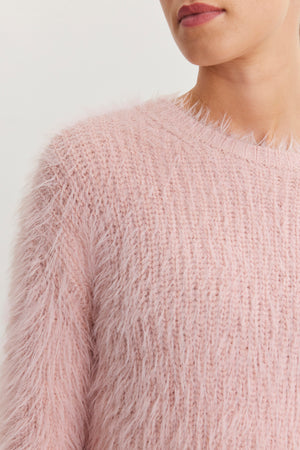 A person is wearing the MAYLIE FEATHER YARN SWEATER from Velvet by Graham & Spencer, showcasing its soft, fuzzy pink texture and crew neckline. The close-up highlights its irresistible feel.