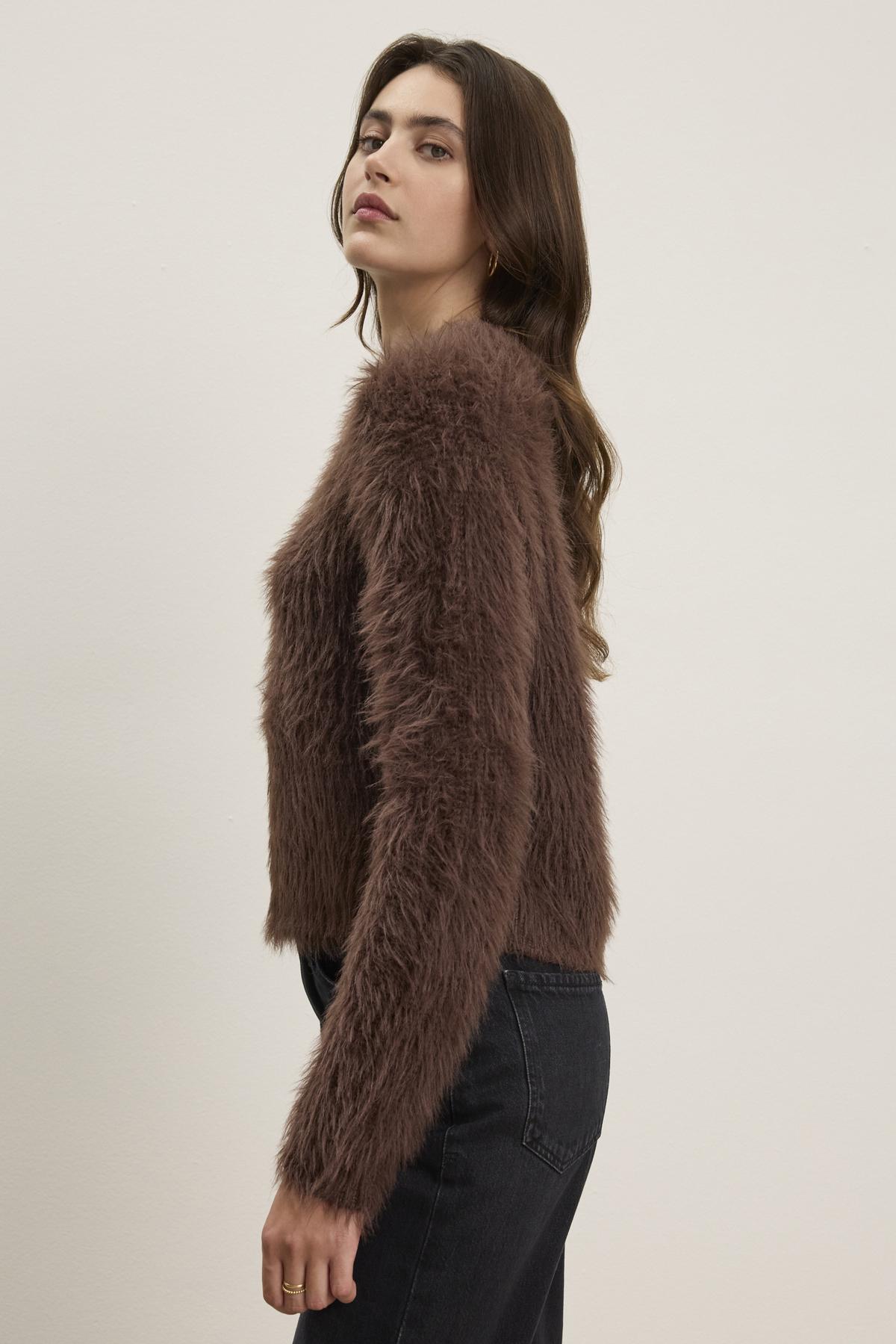   A person poses sideways in front of a plain background, wearing the MAYLIE FEATHER YARN SWEATER by Velvet by Graham & Spencer—a brown, furry long-sleeve top with a crew neckline—paired with black pants. 