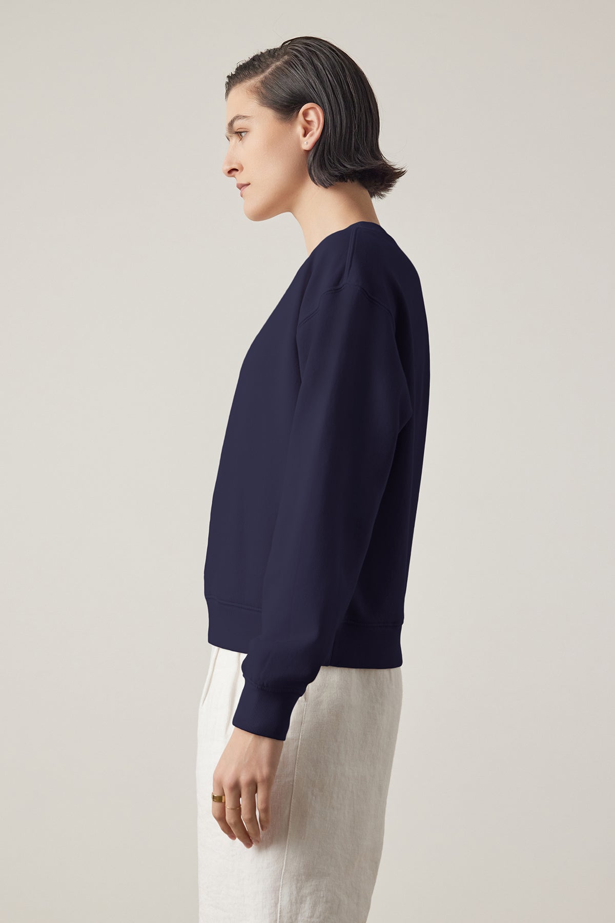   Side profile of a person with slicked-back hair wearing a Navy YNEZ SWEATSHIRT made by Velvet by Jenny Graham and light trousers against a neutral background. 