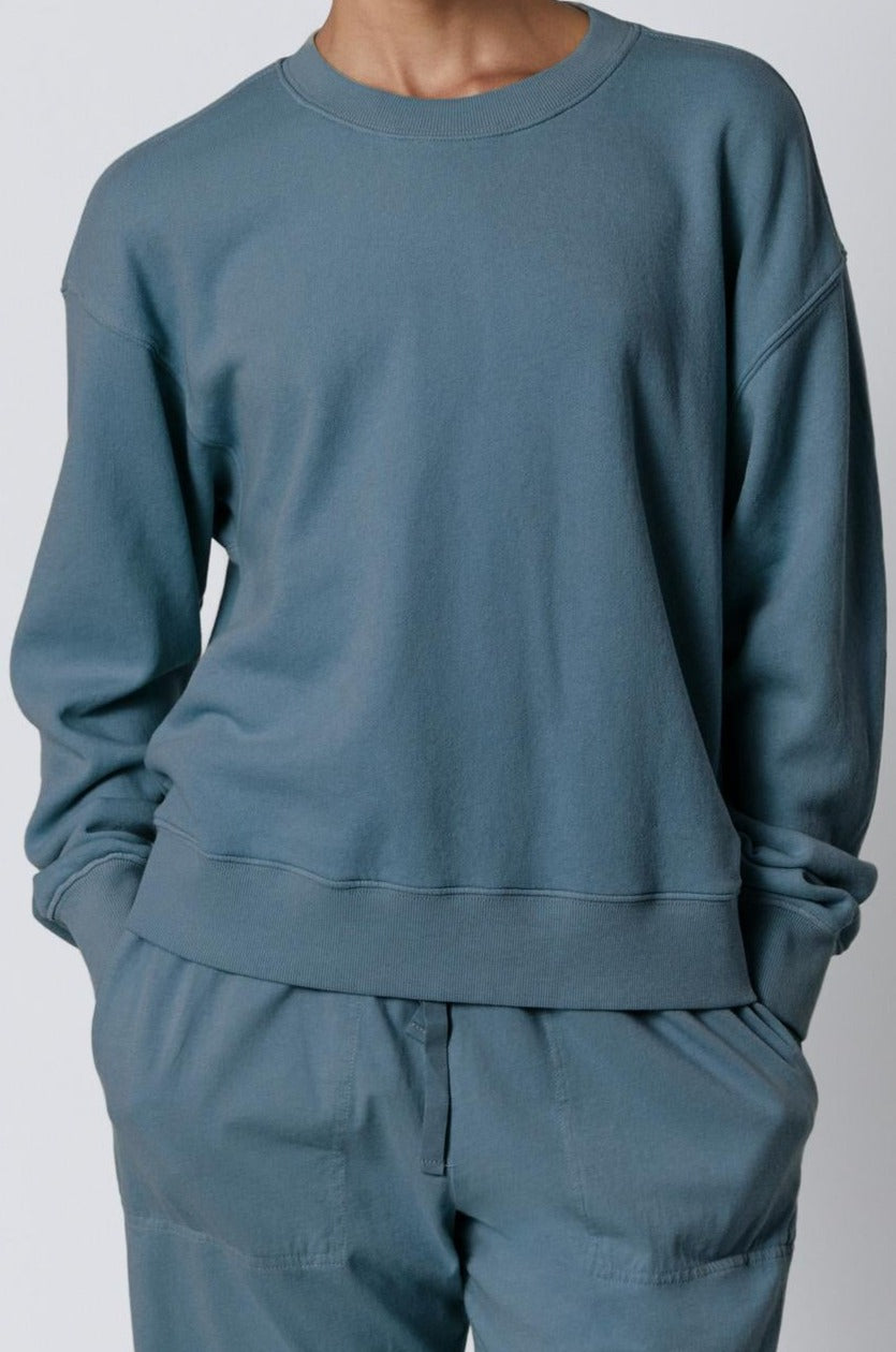   A woman wearing a blue YNEZ Sweatshirt by Velvet by Jenny Graham made of organic cotton and organic fleece. 