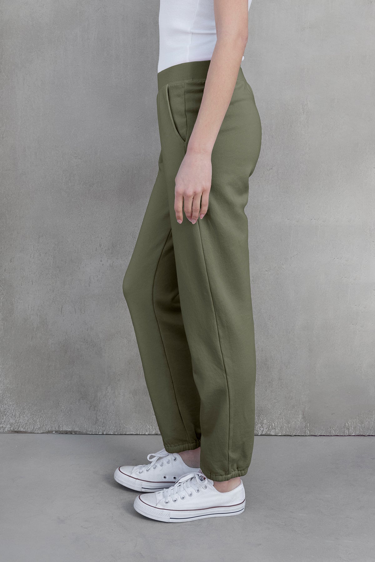   A person wearing Velvet by Jenny Graham's ZUMA SWEATPANT in green and white sneakers stands sideways against a gray background, showcasing sustainable fashion. 