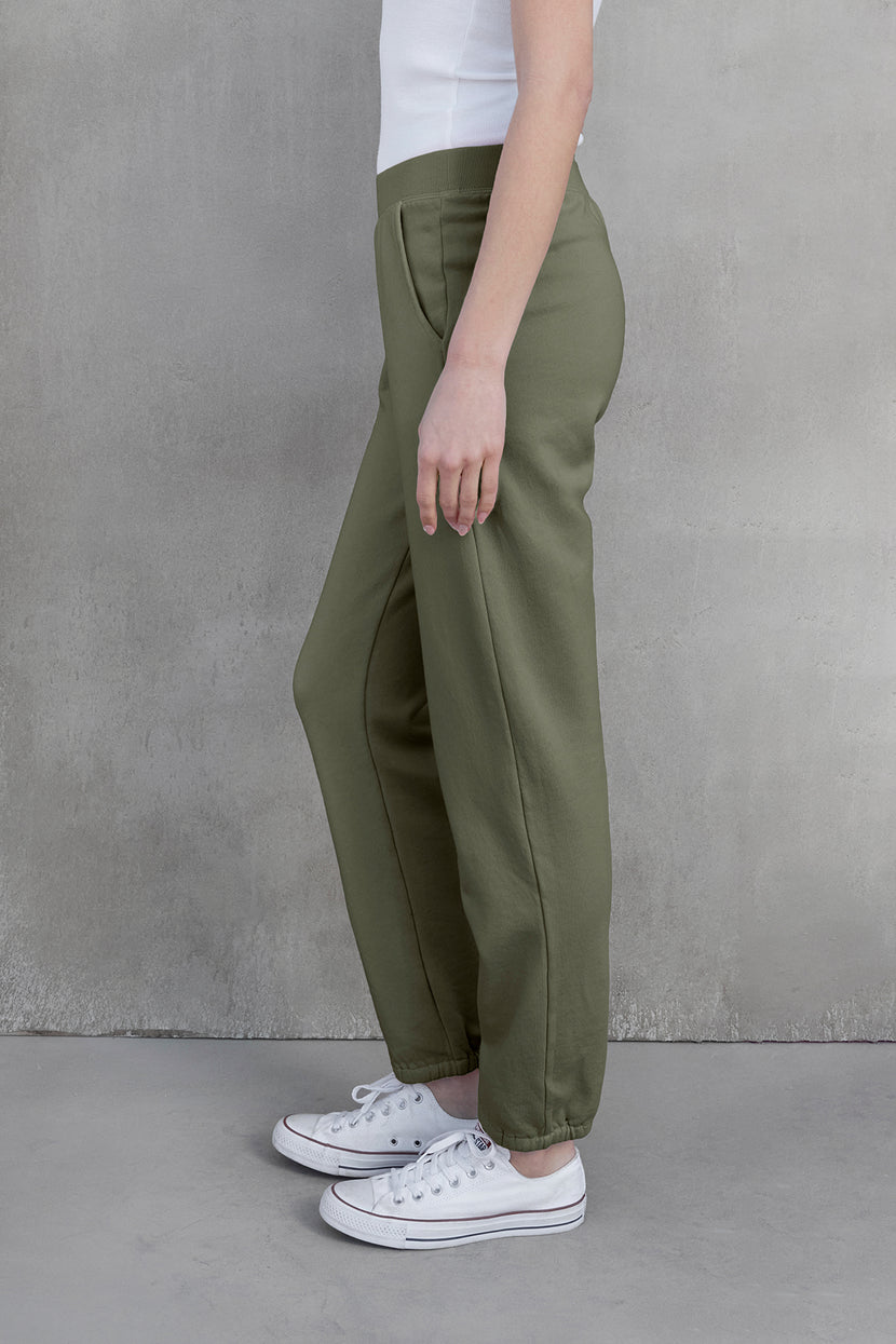 A person wearing Velvet by Jenny Graham's ZUMA SWEATPANT in green and white sneakers stands sideways against a gray background, showcasing sustainable fashion.