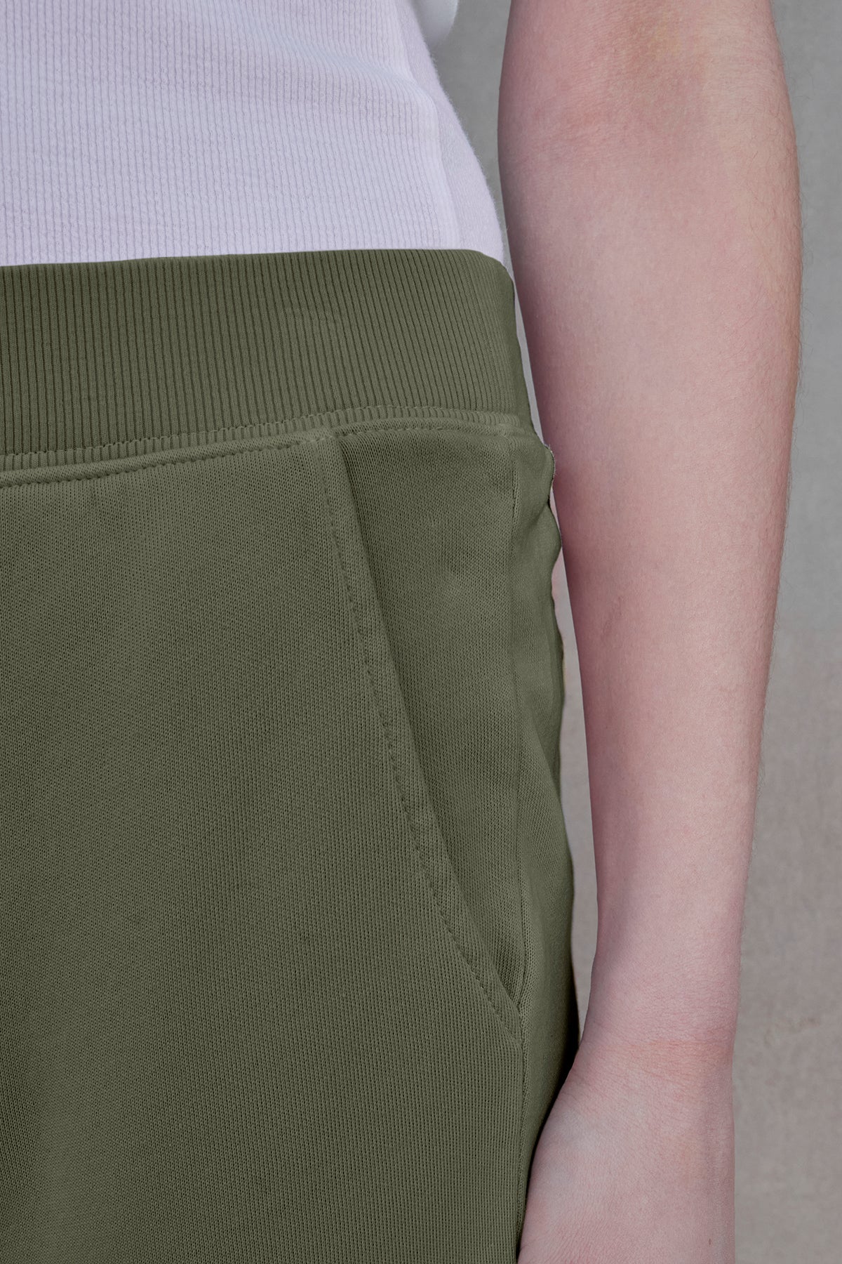   Someone wearing a white shirt and the ZUMA SWEATPANT in olive green by Velvet by Jenny Graham, with their hands relaxed at their side, embodies sustainable fashion. 