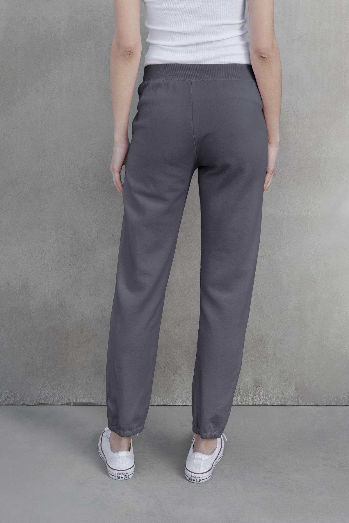   Back view of a person wearing the ZUMA SWEATPANT by Velvet by Jenny Graham and white sneakers, standing against a plain, gray background. 