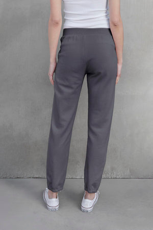 Back view of a person wearing the ZUMA SWEATPANT by Velvet by Jenny Graham and white sneakers, standing against a plain, gray background.