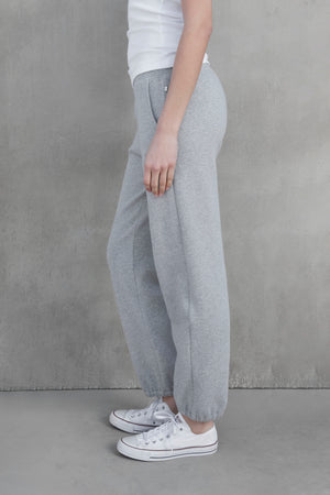 A person in a white shirt and the ZUMA SWEATPANT by Velvet by Jenny Graham stands sideways against a gray concrete wall, wearing white sneakers.