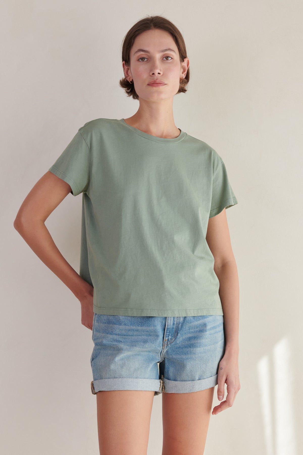   the model is wearing a Velvet by Jenny Graham sage green TOPANGA Tee and denim shorts. 