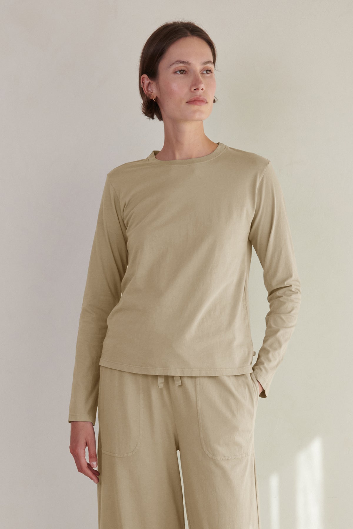   A woman wearing a beige long-sleeved VICENTE TEE and matching pants standing against a neutral background from Velvet by Jenny Graham. 