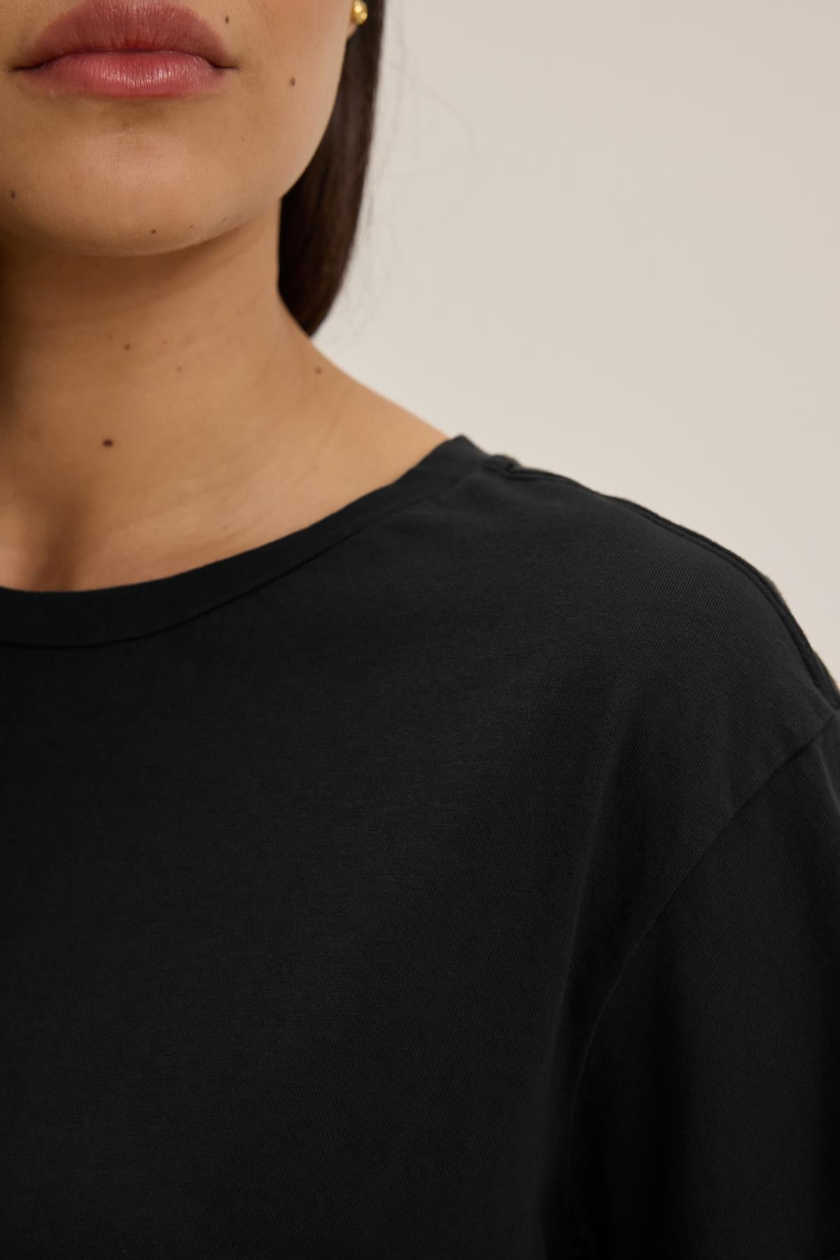 Close-up of a person with long brown hair, wearing a relaxed-fit classic black TOPANGA TEE made of organic cotton by Velvet by Jenny Graham. Only the lower half of the face and shoulder are visible.-37817545195713