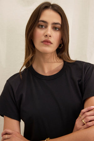 Person with long hair wearing Velvet by Graham & Spencer's JAZZ TEE, a black crew neck t-shirt, and hoop earrings, set against a light-colored background.