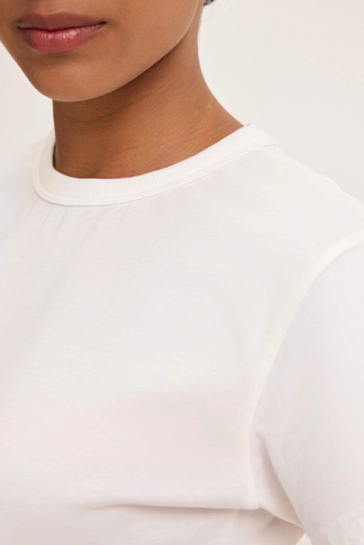 The individual is donning the JAZZ TEE from Velvet by Graham & Spencer, featuring a relaxed boxy silhouette in plain white, partially revealing their face and shoulder against a neutral background.-38819698016449