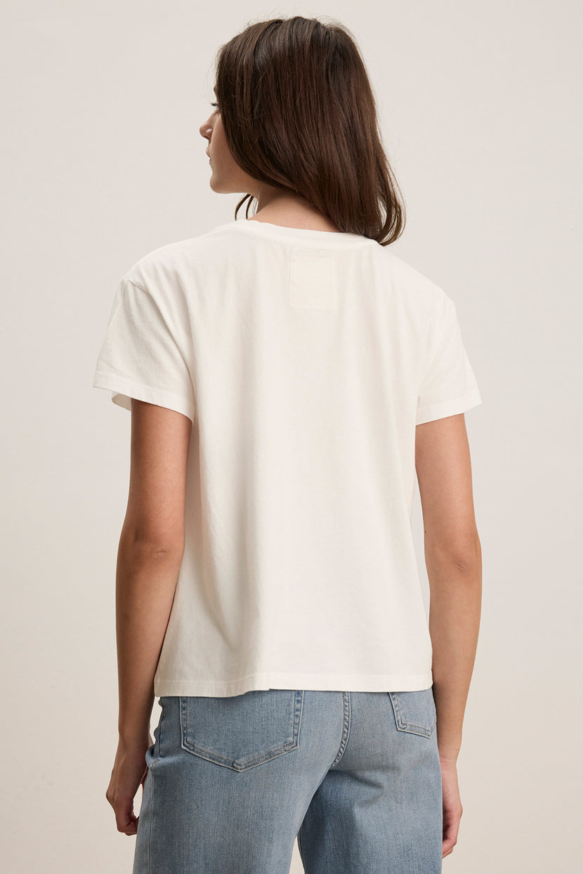 A person in a relaxed-fit TOPANGA TEE by Velvet by Jenny Graham and blue jeans faces away from the camera against a neutral background.