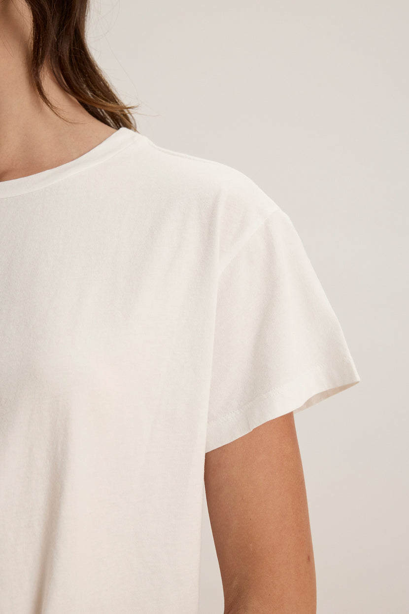 Close-up of an individual in a relaxed-fit white TOPANGA TEE by Velvet by Jenny Graham, showcasing the shoulder and upper torso. Made from organic cotton, it enhances comfort. The background is neutral.