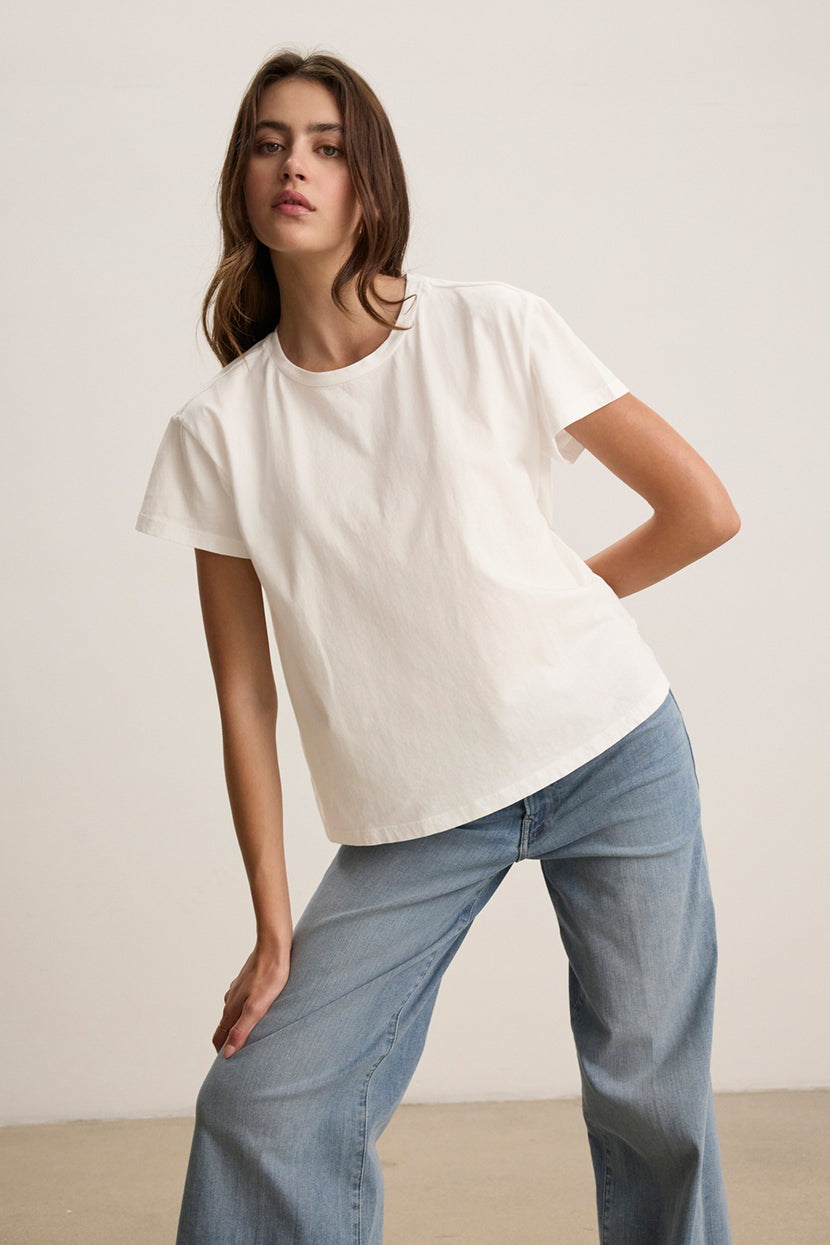 A person wearing the TOPANGA TEE by Velvet by Jenny Graham—an organic cotton, relaxed-fit white t-shirt—and blue jeans poses against a plain background.