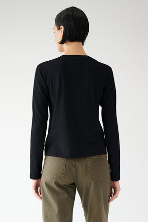 Woman wearing a Velvet by Jenny Graham VICENTE TEE in black and olive pants seen from the back.