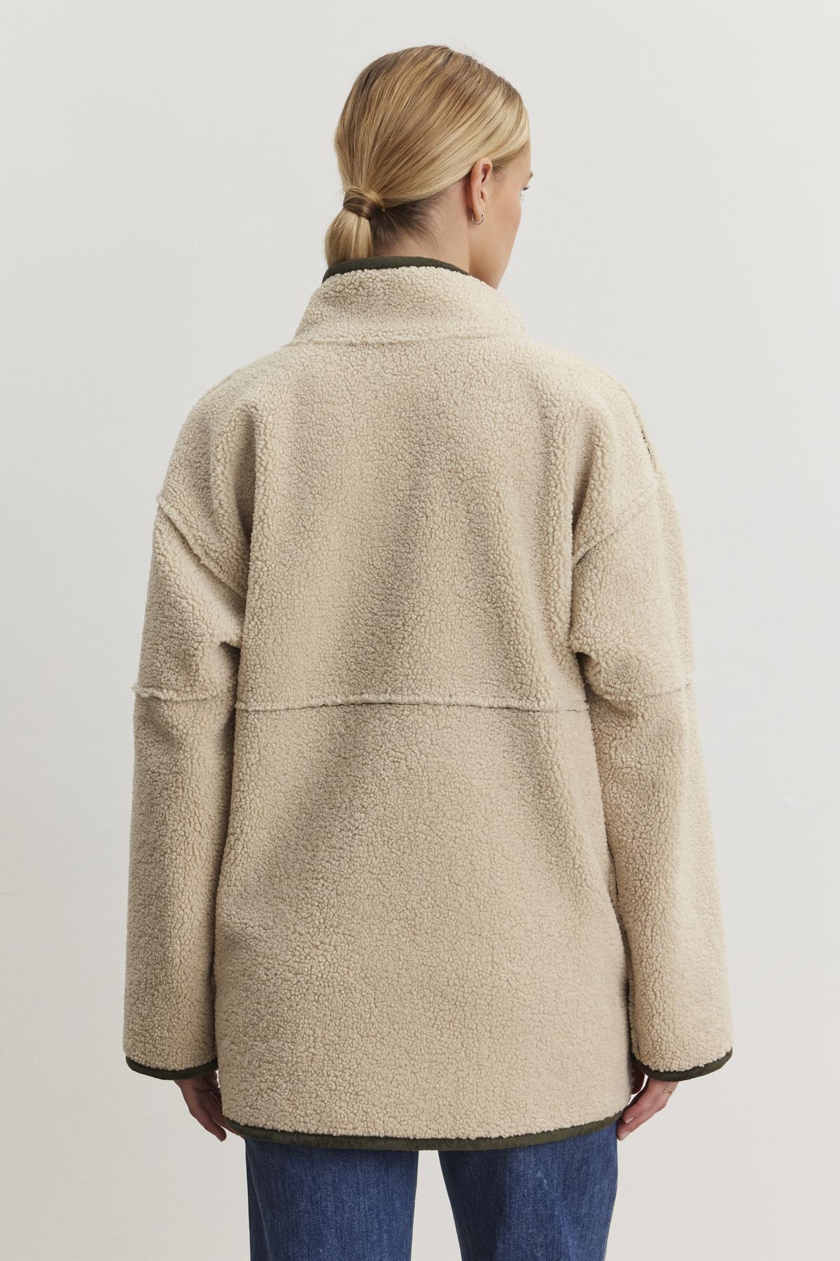   A person wearing the ALBANY LUXE SHERPA REVERSIBLE JACKET by Velvet by Graham & Spencer and a pair of jeans is seen from behind against a neutral background. 