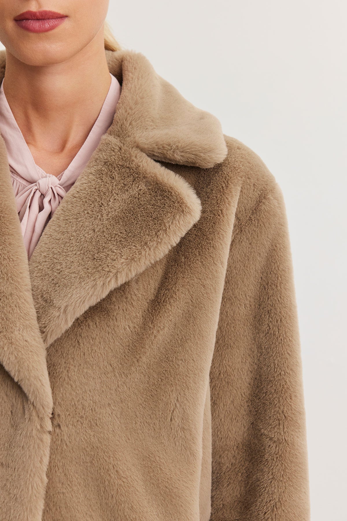 Draped in the EVALYN LUX FAUX FUR COAT by Velvet by Graham & Spencer, one exudes elegance with its soft, light brown allure that transitions effortlessly from day to night, perfectly layered over a pink blouse.-38301345841345