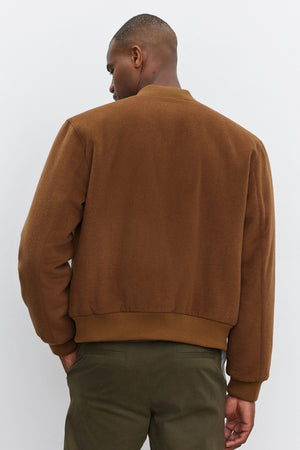 A person is standing with their back to the camera, wearing a FRAZIER BOMBER JACKET by Velvet by Graham & Spencer and green pants, against a plain white background.