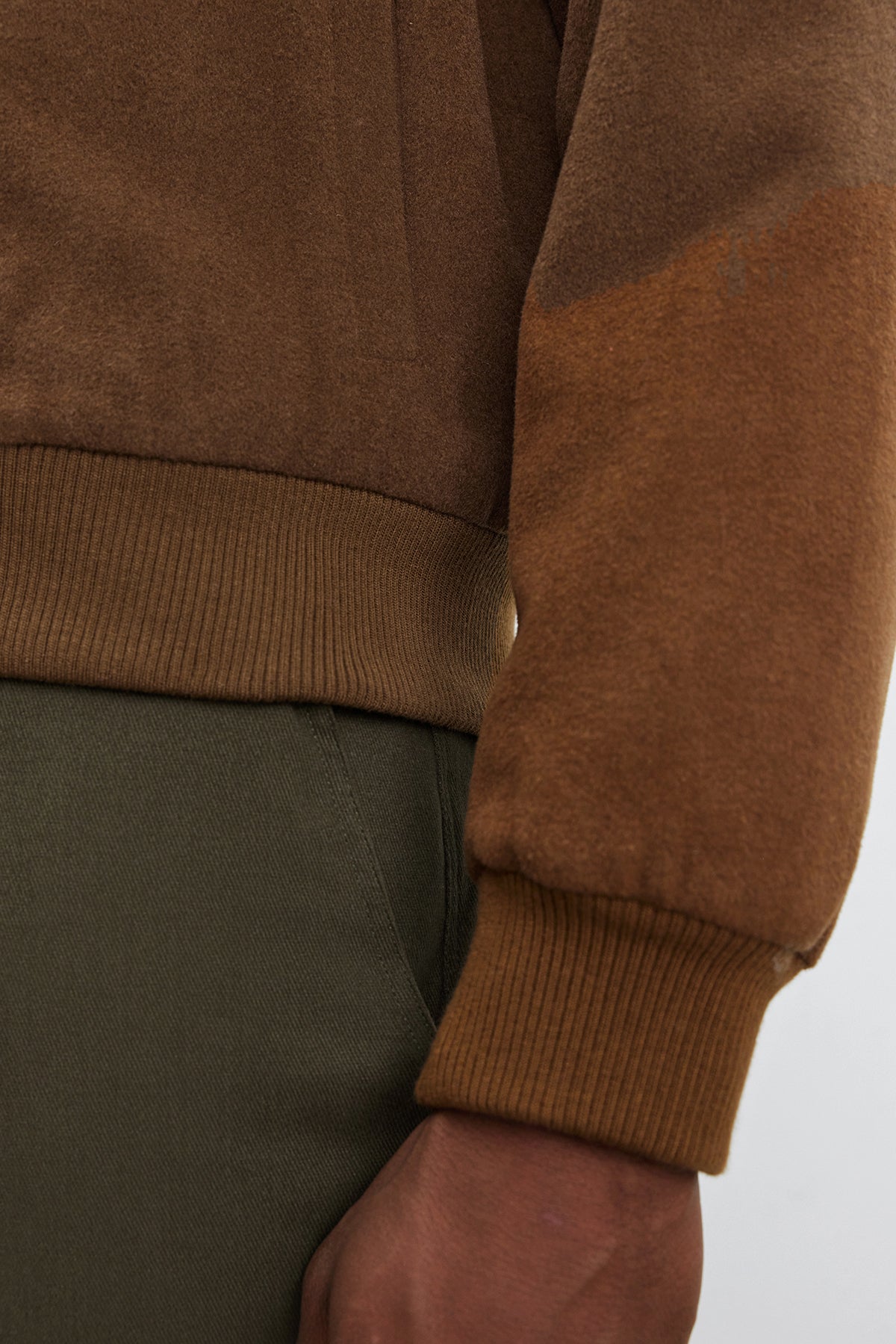   Close-up of a person's arm and torso wearing olive green pants and the Velvet by Graham & Spencer FRAZIER BOMBER JACKET, a brown long-sleeved wool blend shirt with ribbed cuffs, showcasing lasting warmth. 