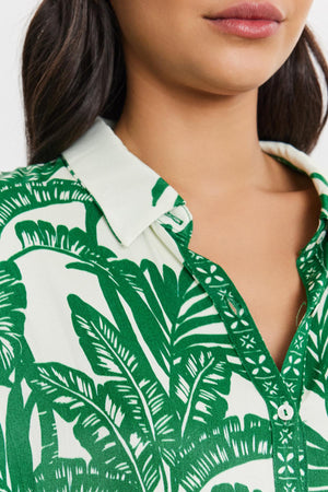 Close-up of a woman wearing a green and white palm print AYLA BUTTON-UP SHIRT by Velvet by Graham & Spencer, focusing on the collar and top buttons.