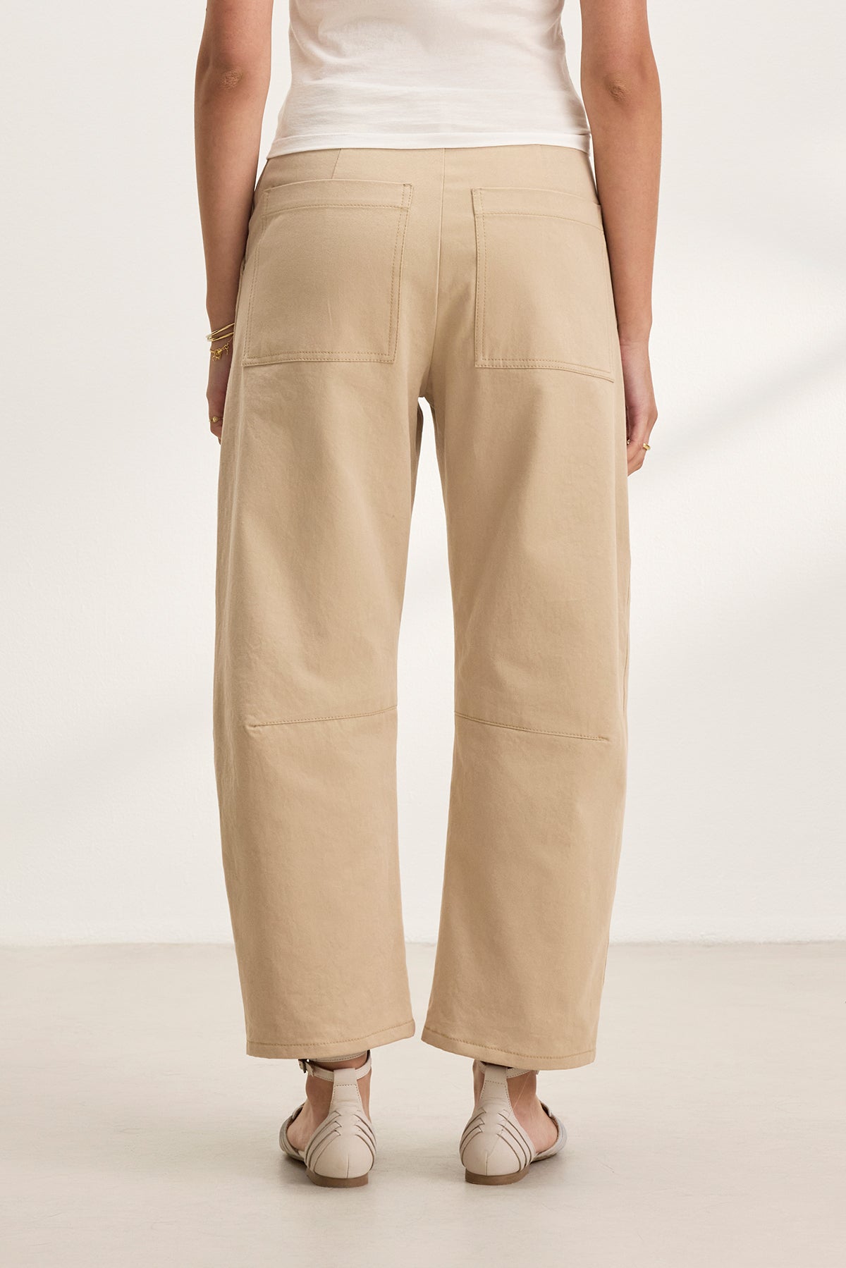   Rear view of a person wearing Velvet by Graham & Spencer's ALEXIS PANT in beige cotton twill, cropped at the ankle, with a white top on a light floor. 