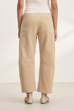 Rear view of a person wearing Velvet by Graham & Spencer's ALEXIS PANT in beige cotton twill, cropped at the ankle, with a white top on a light floor.