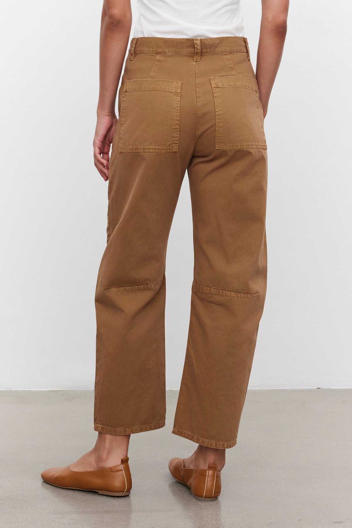 A person wearing the BRYLIE SANDED TWILL UTILITY PANT by Velvet by Graham & Spencer, which features large patch pockets, along with a white top, is seen from the back standing on a light-colored floor.-37676285657281