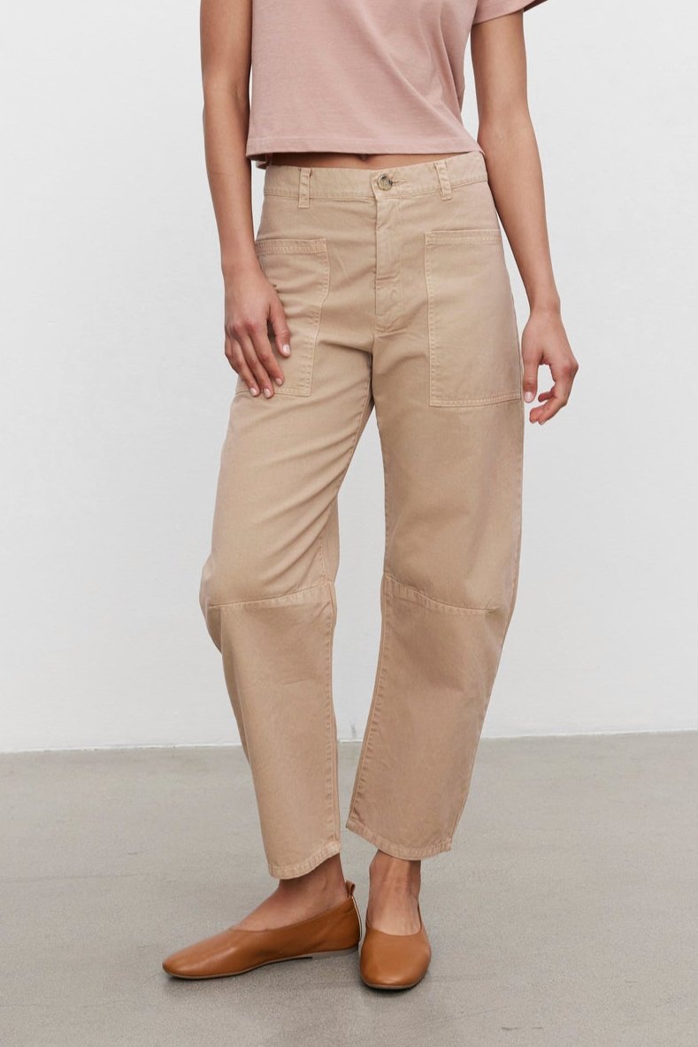   Person standing against a plain white background, wearing a light pink t-shirt paired with the BRYLIE SANDED TWILL UTILITY PANT in beige cotton twill by Velvet by Graham & Spencer, and brown shoes. 