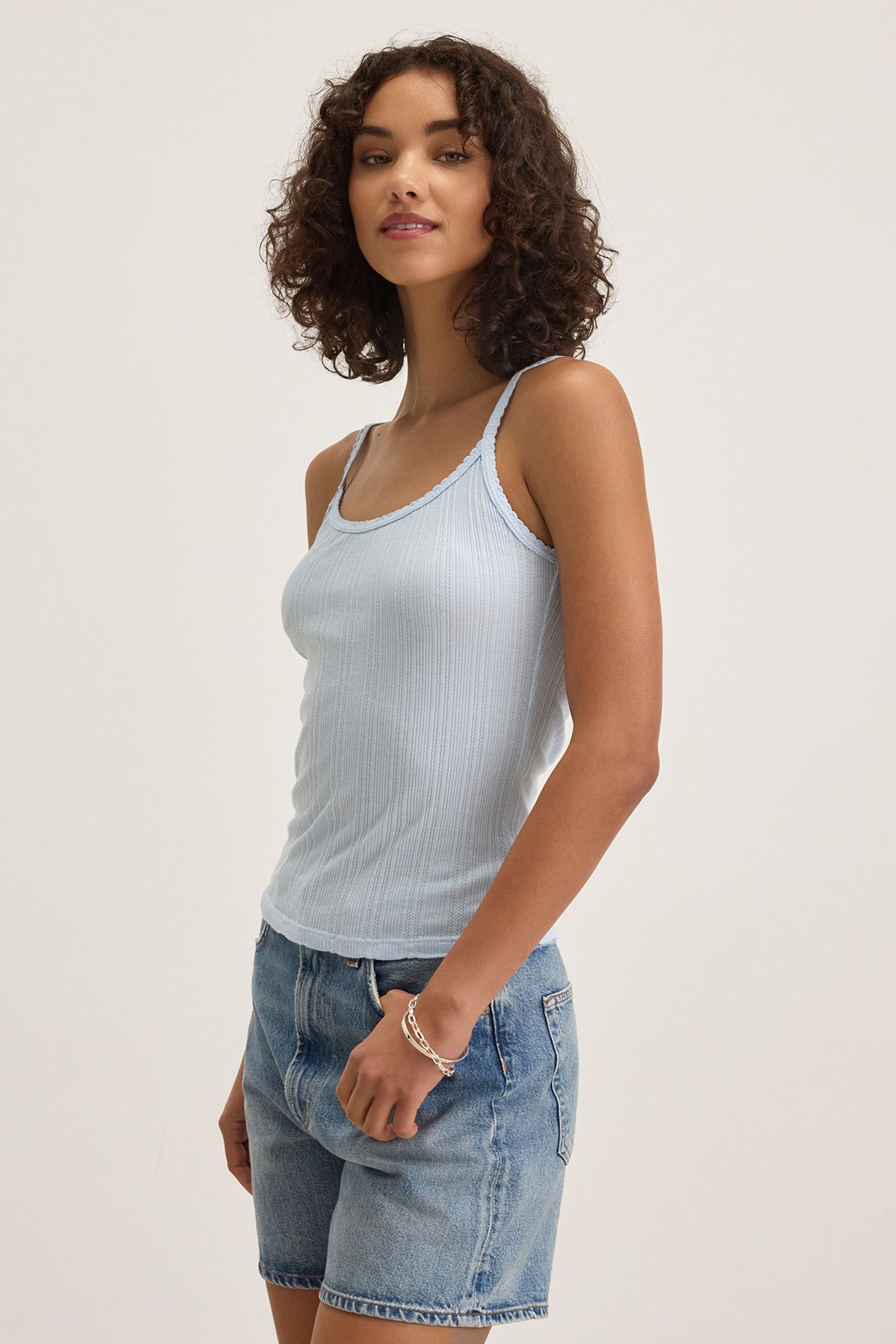   A person in the INIKU TANK TOP by Velvet by Graham & Spencer and denim shorts, standing and smiling against a plain background. 