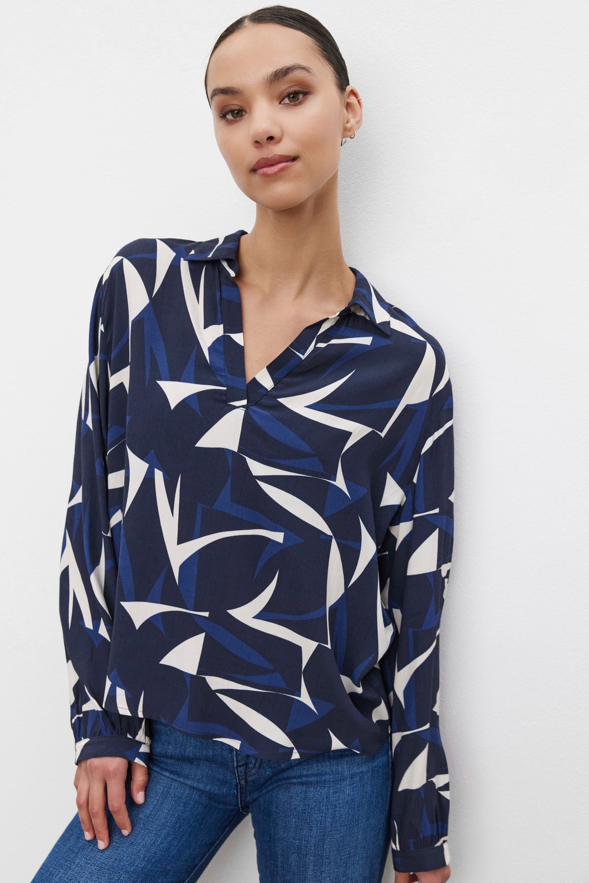 Person wearing the CARAH TOP from Velvet by Graham & Spencer, which features a blue and white patterned blouse with a split neck and textured fabric, paired with jeans, stands against a plain white background.-37676901925057