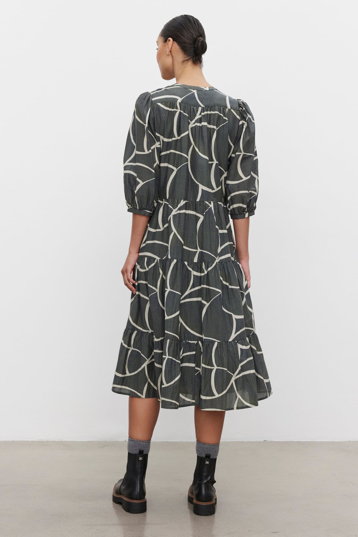   Person standing indoors facing away, wearing the JOHANNA PRINTED SILK COTTON VOILE DRESS by Velvet by Graham & Spencer, black ankle boots, and dark socks. 