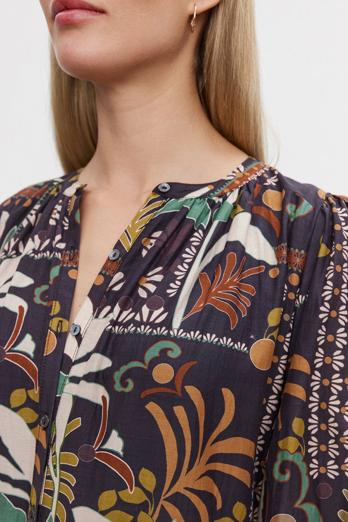   A person with long, blond hair is wearing the JOHANNA PRINTED SILK COTTON VOILE DRESS by Velvet by Graham & Spencer, featuring a multicolored pattern, a round neckline, and a button front placket. They pair it elegantly with a three-tiered skirt. 