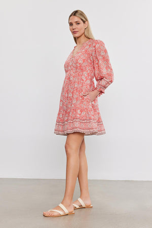 Woman in a floral print cotton voile Velvet by Graham & Spencer MARY DRESS and white sandals standing against a plain background.