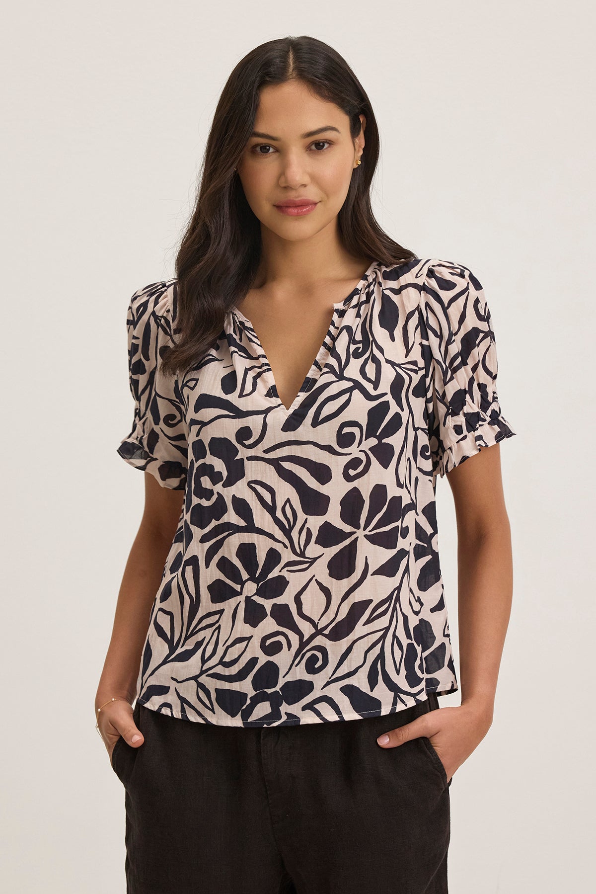 A person wearing the LESLIE TOP by Velvet by Graham & Spencer, featuring a floral pattern, stands with hands in pockets against a plain background.-38754090221761