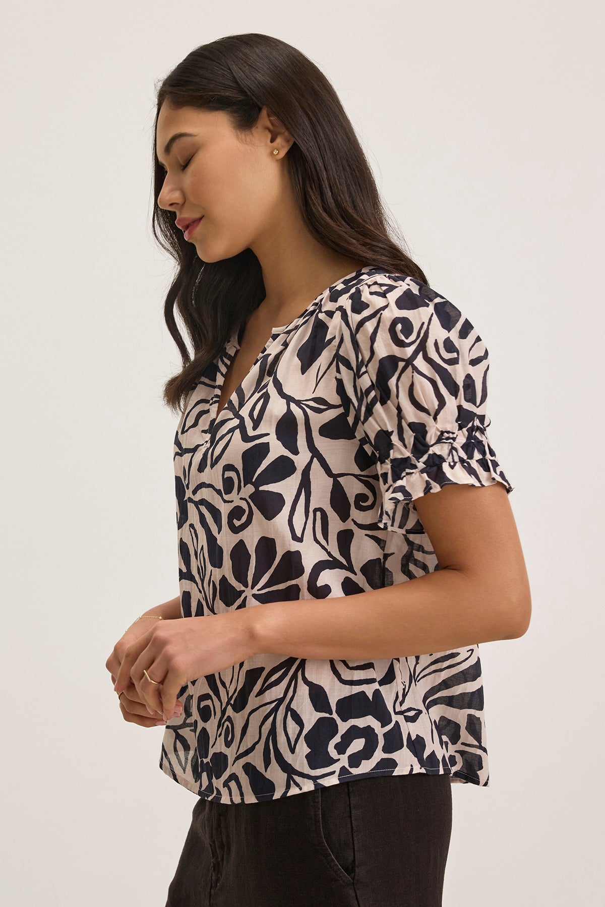   A woman in profile wears the Velvet by Graham & Spencer LESLIE TOP, featuring a leaf pattern and short sleeves, set against a plain background. 