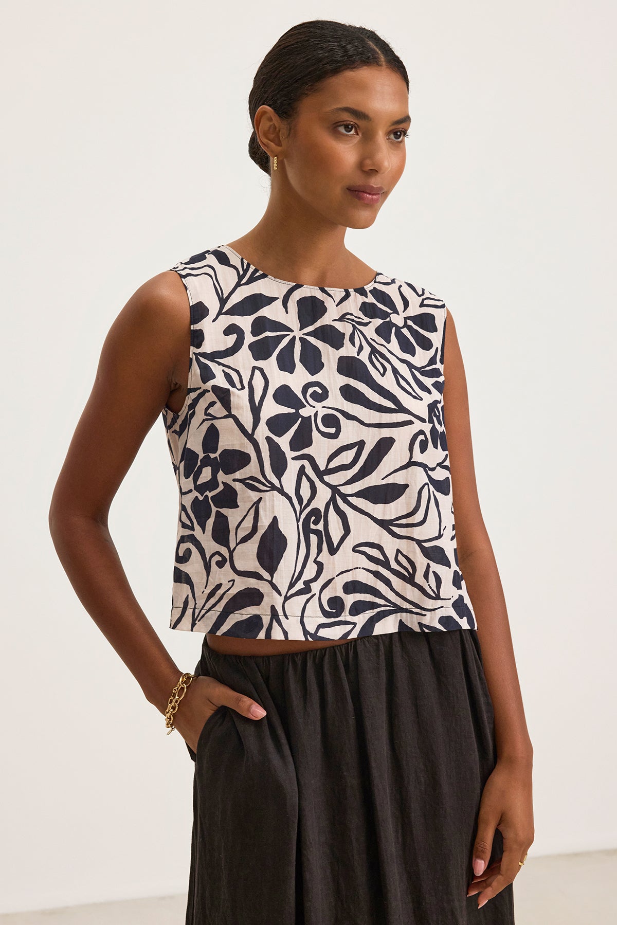   A person dons the chic NAEEM TOP from Velvet by Graham & Spencer, featuring black leaf patterns, paired with a black skirt, against a plain backdrop. 