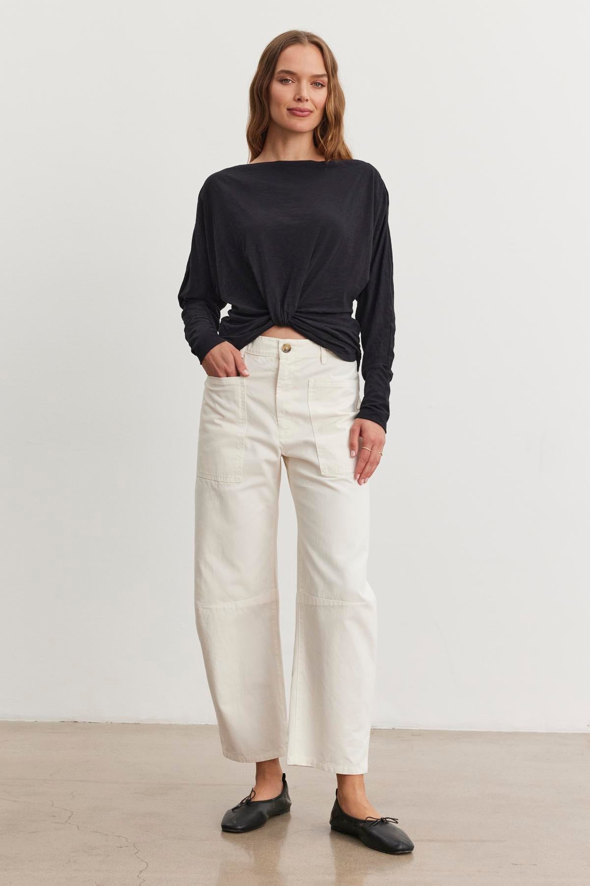 A person stands against a plain background wearing a black long-sleeve top, BRYLIE SANDED TWILL UTILITY PANT by Velvet by Graham & Spencer in white cotton, and black shoes.-38512513712321