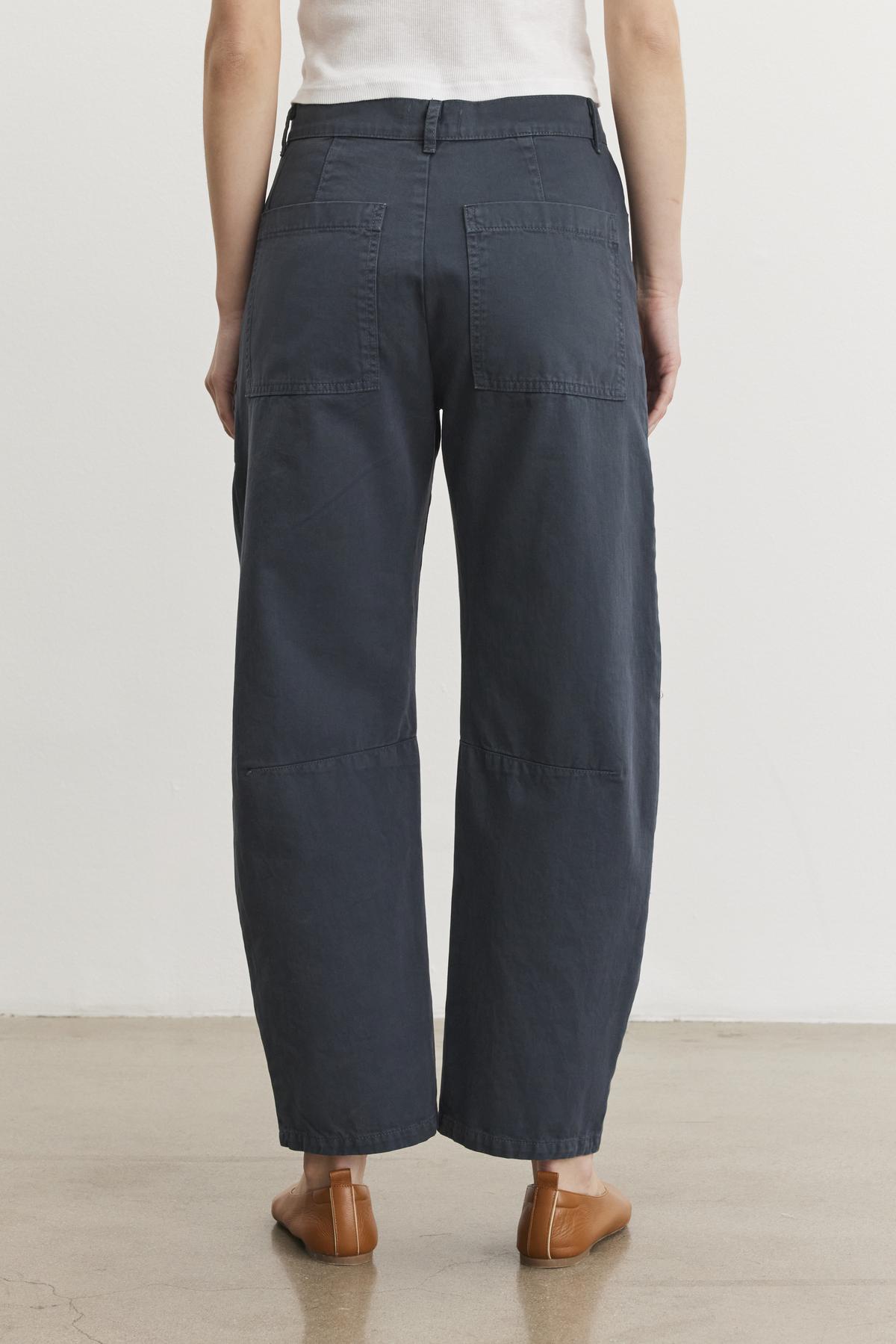 A person is wearing Velvet by Graham & Spencer's BRYLIE SANDED TWILL UTILITY PANT in navy with patch pockets, paired with brown shoes, facing away.-38512693084353