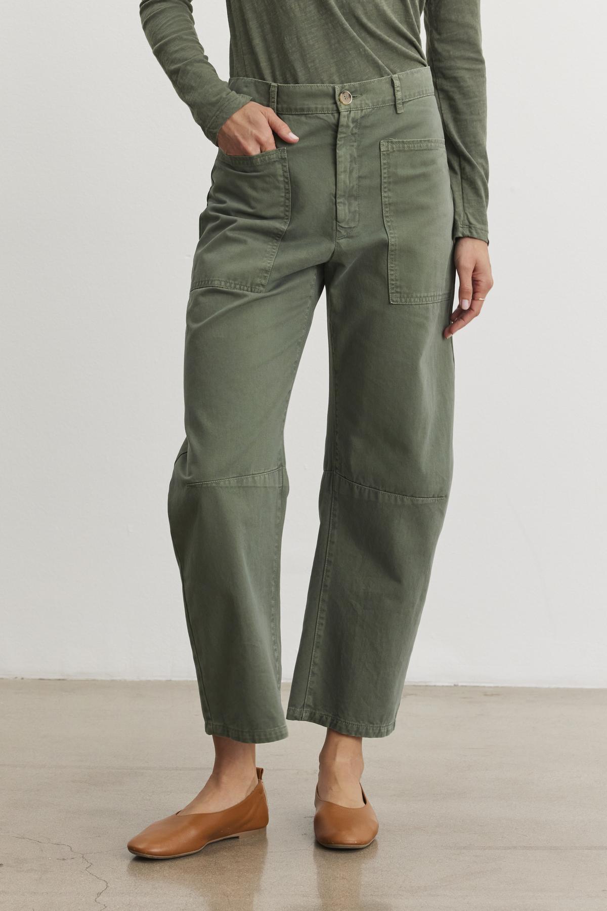   Someone in a green long-sleeve shirt and Velvet by Graham & Spencer's BRYLIE SANDED TWILL UTILITY PANT stands on a polished concrete floor, wearing tan flat shoes. 