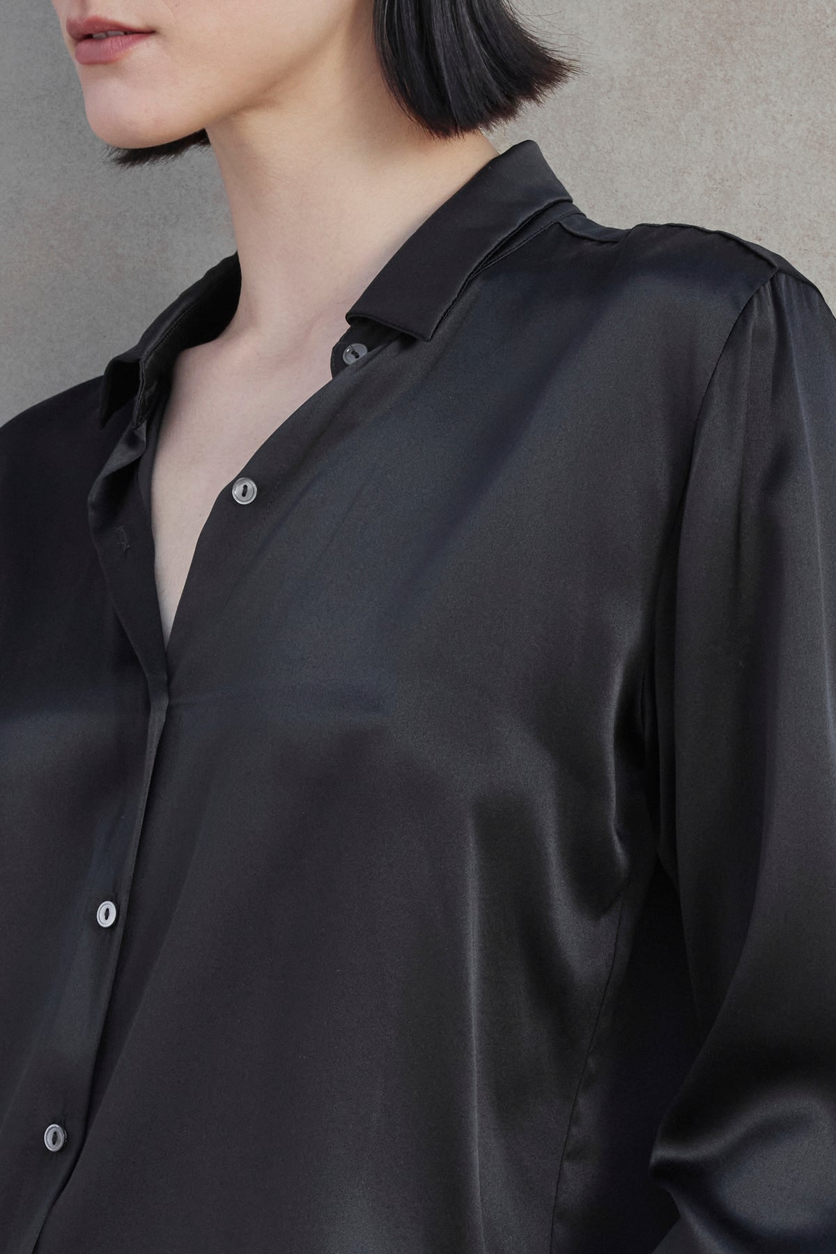 Close-up of the upper body of a person wearing the CALABASAS SILK CHARMEUSE BLOUSE by Velvet by Jenny Graham, featuring a partially open collar, standing against a light brown background.-37659913912513