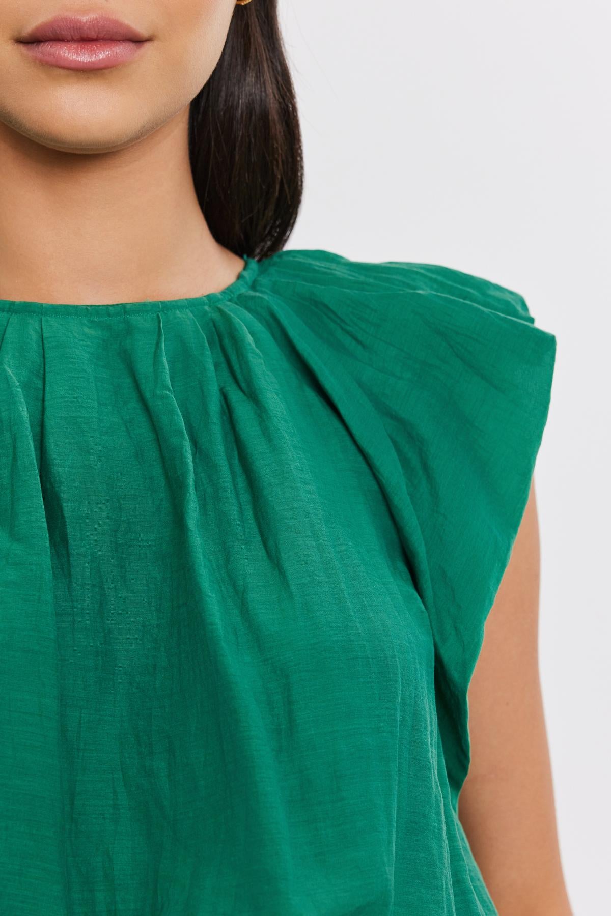 Close-up of a woman wearing a green silk cotton voile AMORA TOP by Velvet by Graham & Spencer with gathered detailing at the shoulder. Only the lower half of her face and shoulder are visible.-36910240465089