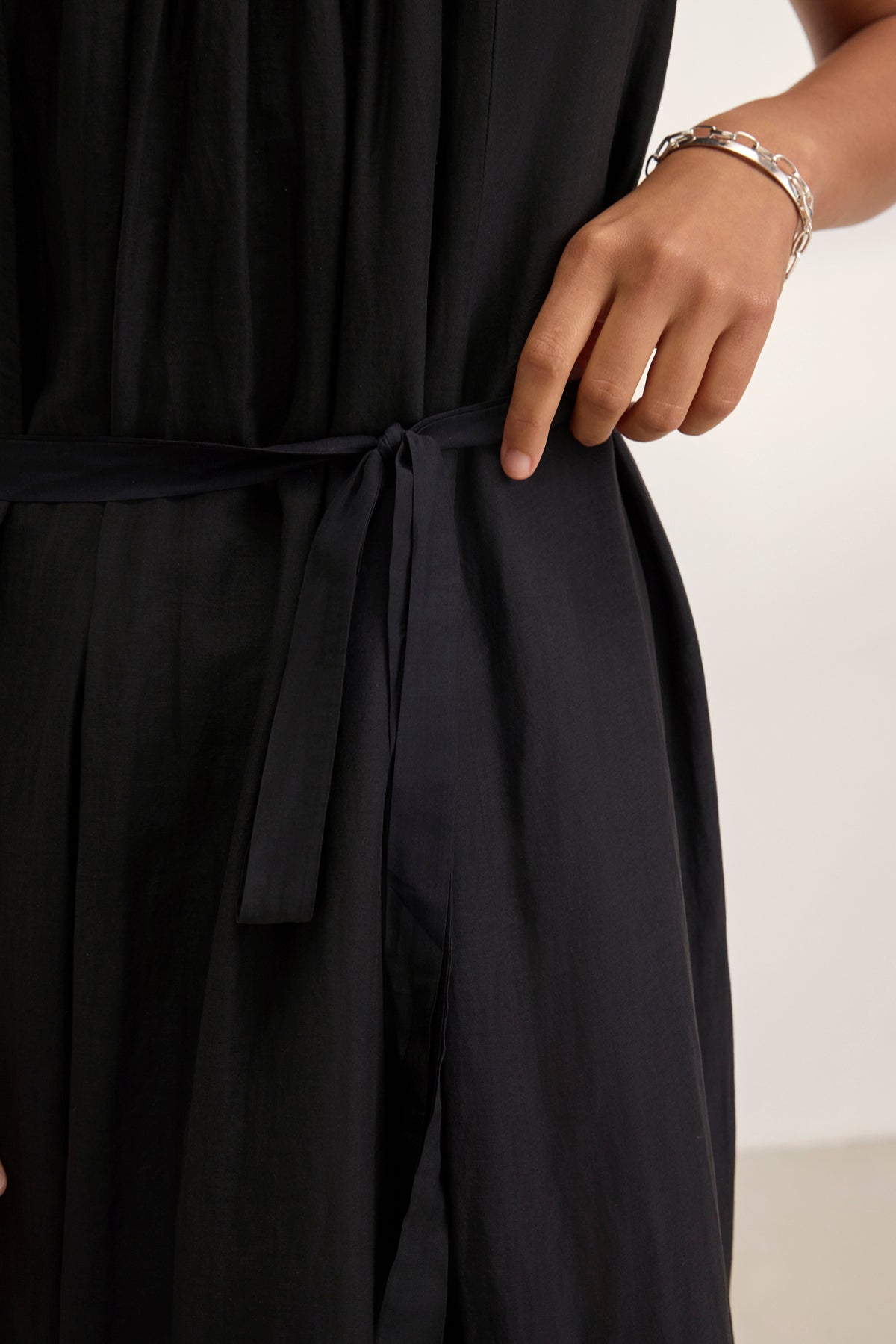   Elegantly dressed in a BAYOU SILK COTTON VOILE DRESS by Velvet by Graham & Spencer, a person gracefully adjusts the waist tie with one hand and wears a silver bracelet on the other wrist. 