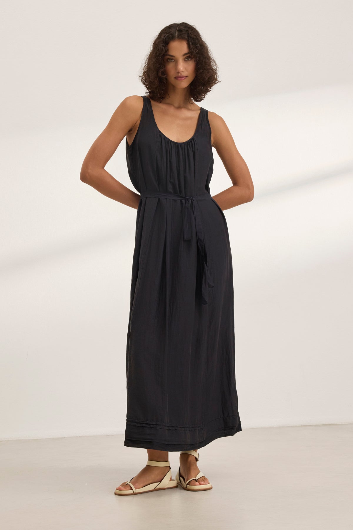   A person models the BAYOU SILK COTTON VOILE DRESS by Velvet by Graham & Spencer, a sleeveless black maxi paired with sandals, set against a white backdrop for versatile styling. 