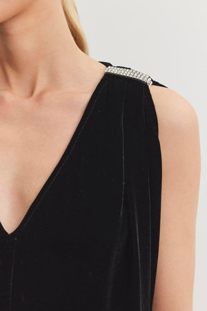 A woman wearing a sleeveless black top adorned with rhinestone accents on the shoulder and featuring a sophisticated v-neckline from Velvet by Graham & Spencer.