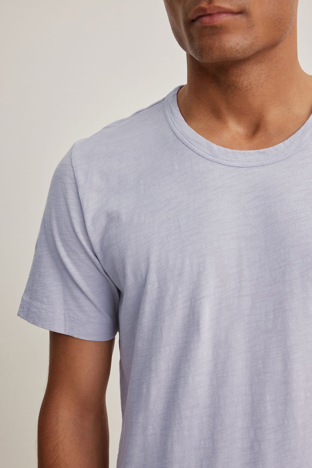   A person wearing the AMARO TEE in light gray from Velvet by Graham & Spencer, made of soft Peruvian cotton. The image shows an upper body with a classic crew neckline, making it ideal as a versatile layering piece. 