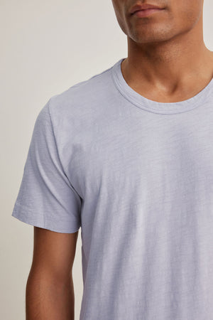 A person wearing the AMARO TEE in light gray from Velvet by Graham & Spencer, made of soft Peruvian cotton. The image shows an upper body with a classic crew neckline, making it ideal as a versatile layering piece.