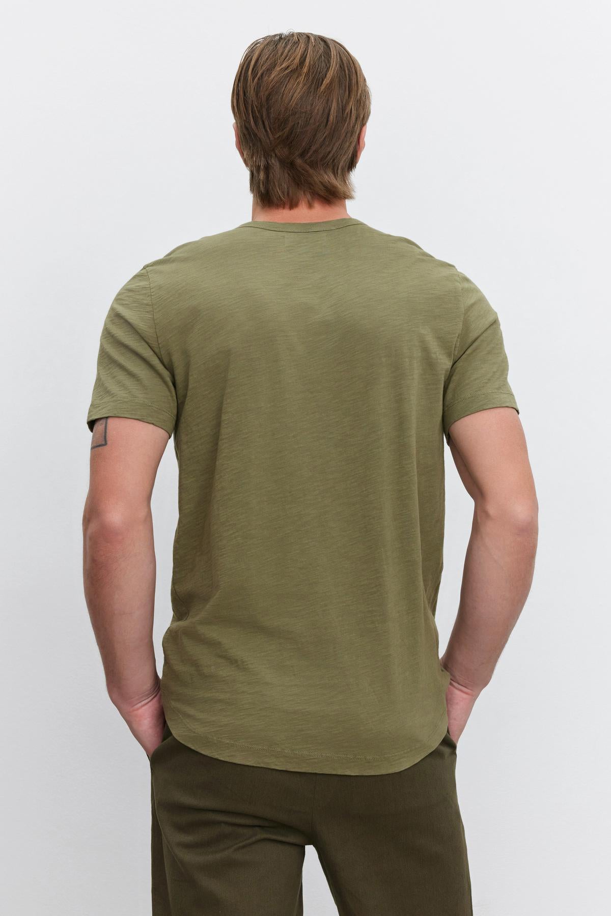 A person with light brown hair wearing an olive green AMARO TEE by Velvet by Graham & Spencer and dark green pants is standing with their back to the camera.-37682021826753