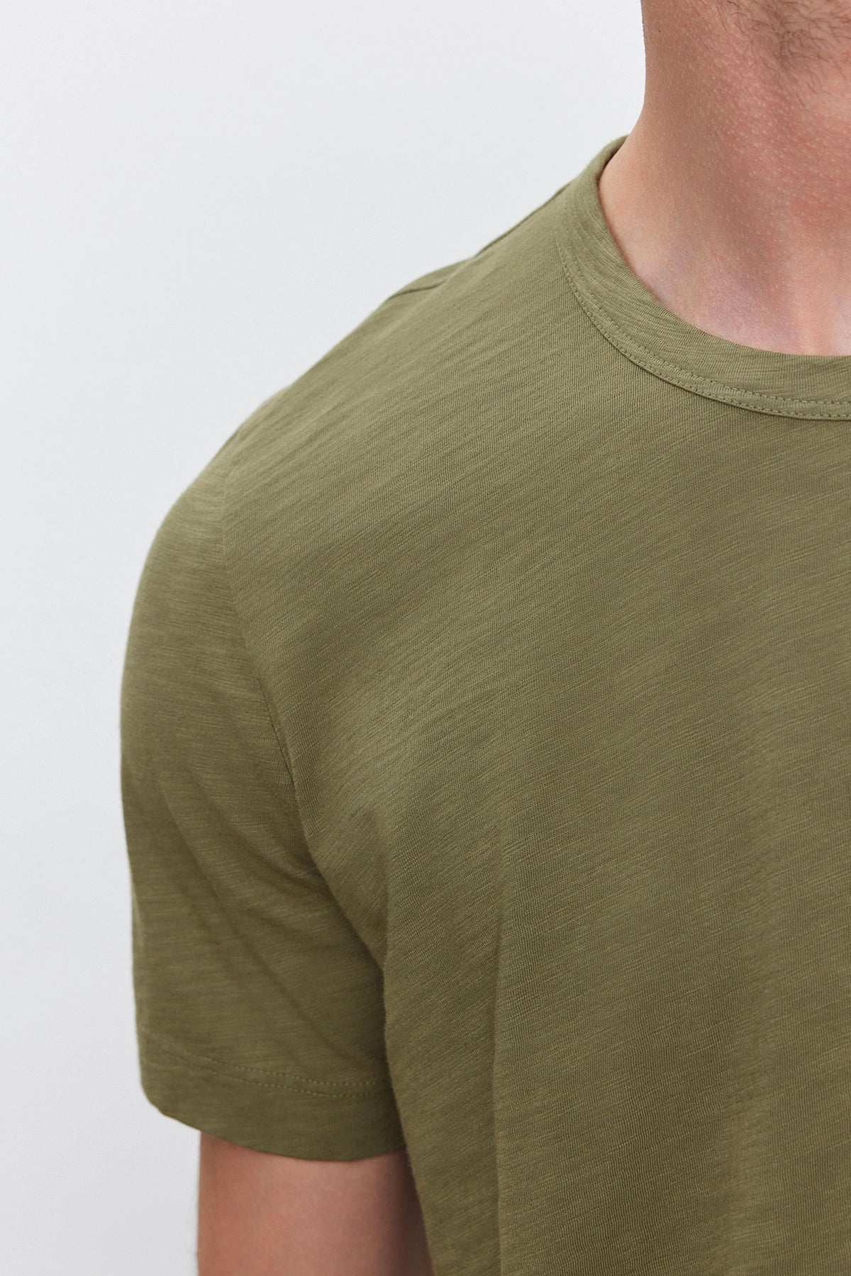 A person wearing the AMARO TEE by Velvet by Graham & Spencer, a plain green short-sleeve t-shirt with a classic crew neckline, shown from the neck to the shoulder against a white background.-37682021892289