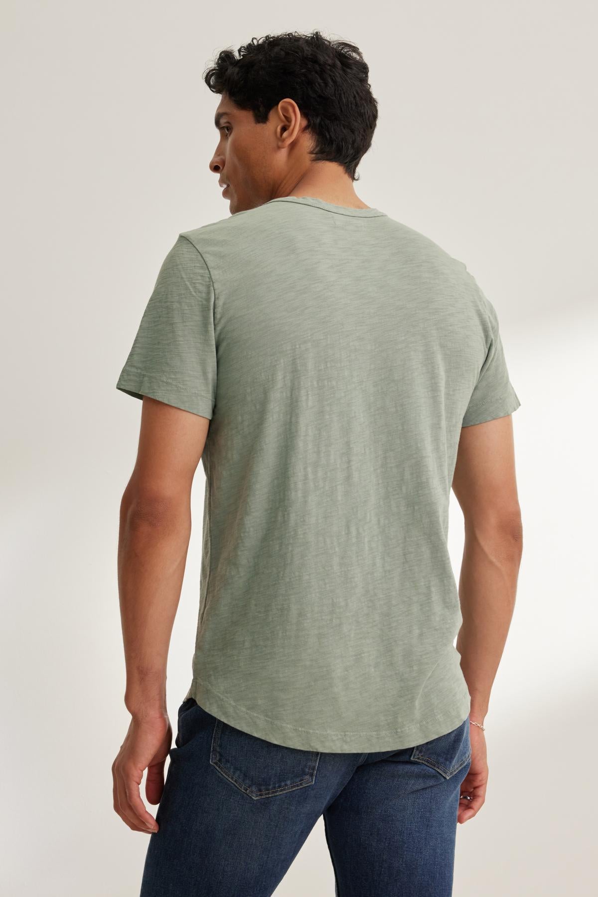 A man with short dark hair, seen from the back, wears the AMARO TEE by Velvet by Graham & Spencer. The light green T-shirt has a classic crew neckline and is made of lightweight Peruvian cotton. He pairs it with blue jeans.-38643226804417