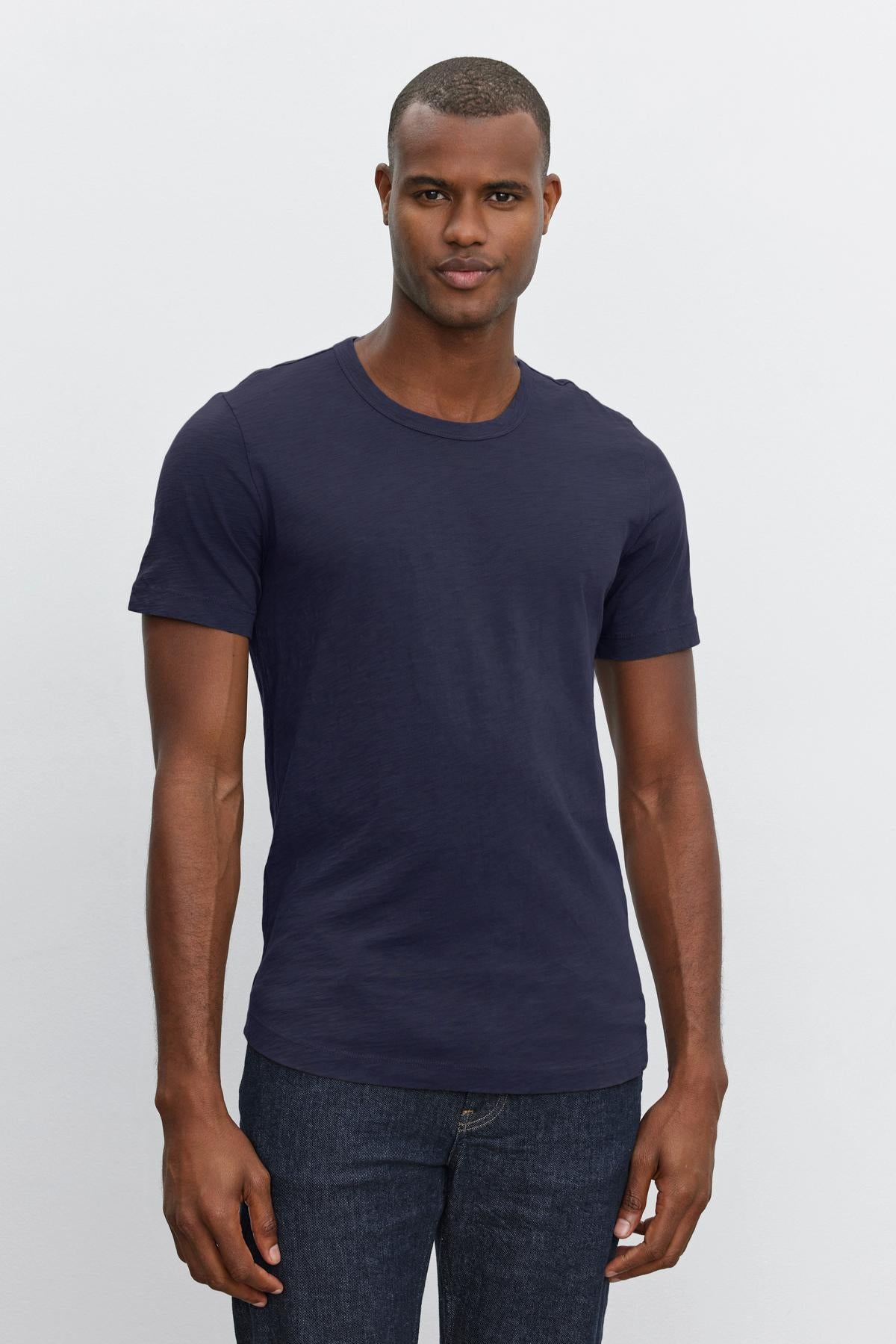   Man wearing a navy blue Velvet by Graham & Spencer AMARO TEE and jeans standing against a plain background. 